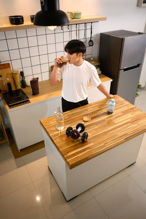 Fit young man drinking a protein shake in a stylish kitchen after exercising.の写真素材