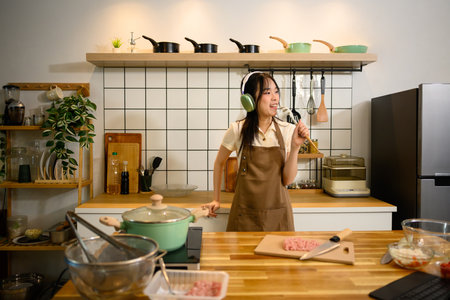 Cheerful woman wearing head phone singing while cooking in a stylish kitchen.の写真素材