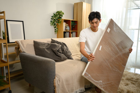 Man unwrapping a wooden table panel during a furniture assembly in living room.の写真素材