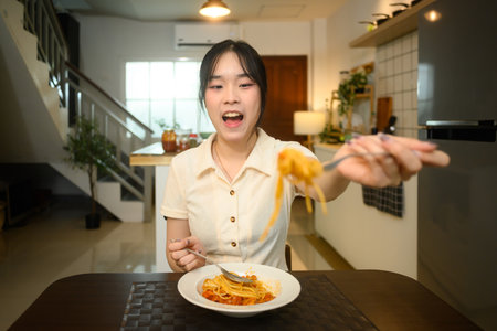 Young woman enjoying a homemade spaghetti meal at a dining table.の写真素材