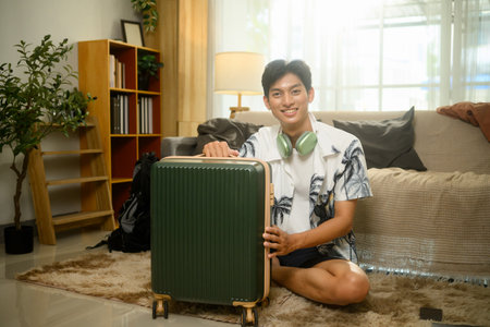 Cheerful young asian man packing his suitcase for a summer trip.の写真素材