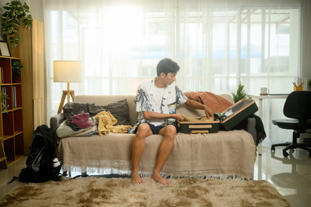 Cheerful young man in a tropical shirt packing his suitcase for summer trip.の写真素材