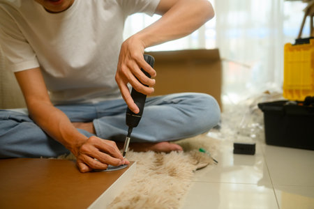 Man using power screwdriver to assembling piece of furniture at home.