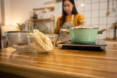 Glass bowl filled with dry instant noodles on a wooden countertop, ready to be cooked.の写真素材
