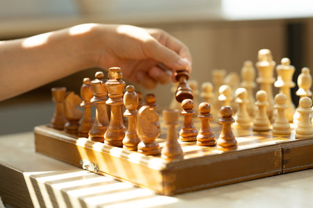 Hand holding chess piece, making a move on a classic wooden chessboard.