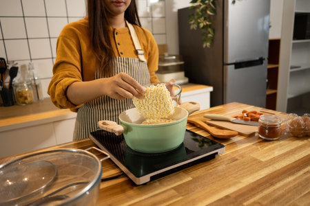 Close up shot of woman putting dried instant noodles into a boiling pot.の写真素材