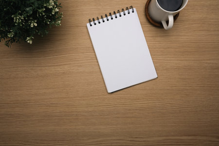 Wooden desk with a notepad, potted plant and a warm cup of coffee.の写真素材