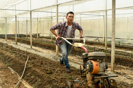 Farmer tilling soil in a greenhouse preparing the land for planting.の写真素材