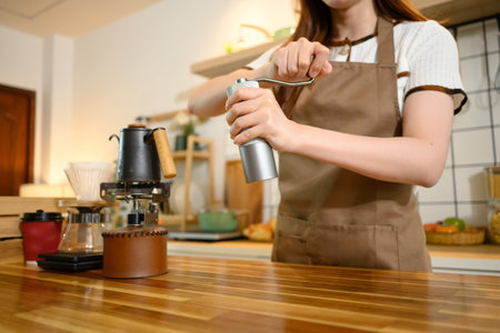 Close up of a woman using manual coffee grinder while preparing fresh coffee in a warm kitchen.の写真素材