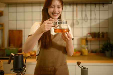 Smiling woman holding a glass carafe filled with freshly brewed coffee, standing in a cozy kitchen.の写真素材