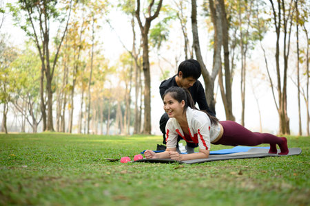 Strong young woman doing plank pose outdoors with trainer assistance.の写真素材