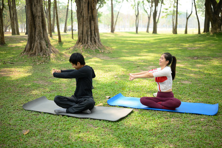 Man and woman stretching exercise on yoga mats in a serene outdoor park.