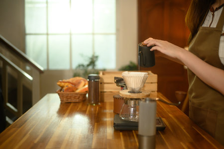 Close up of woman pouring hot water into a coffee dripper on a wooden kitchen counter.の写真素材