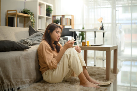 Sad woman holding a medicine bottle while sitting on the floor. Mental Health concept.の写真素材