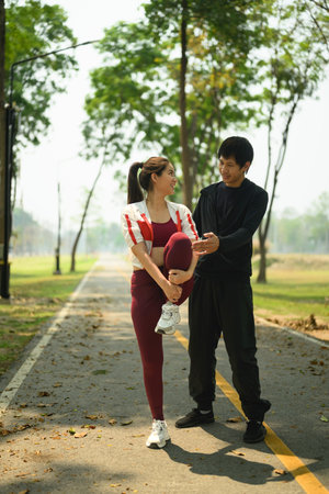 Young man assisting his partner stretching before run or workout on a peaceful path. Healthy...