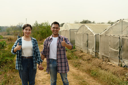 Successful farmers standing in front of a greenhouse, giving thumbs up. Concept of successful...