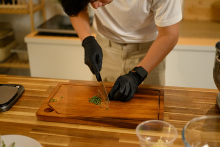 Close up of man chopping fresh parsley on wooden cutting board while preparing homemade garlic butter in a kitchen.の写真素材