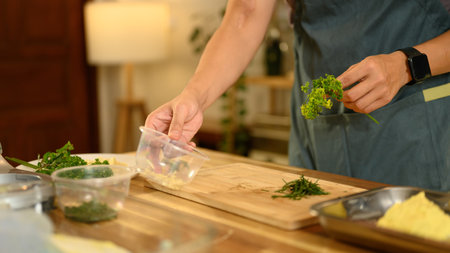 Young man wearing an apron preparing fresh herbs for compound butter.