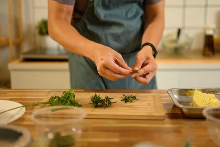 Young man wearing an apron preparing fresh herbs for compound butter.