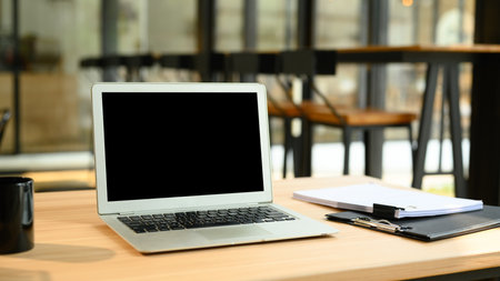 Laptop with empty screen, financial document and coffee cup on wooden desk.の写真素材