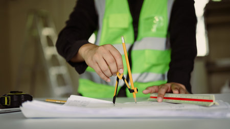 Close up of an architect using a compass to draw precise measurements on blueprints.