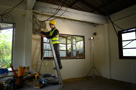 Electrician wearing yellow hard hat working on wall wiring at a construction site.