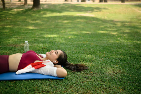 Carefree young woman listening to music while resting on yoga mat in a sunny park.の写真素材