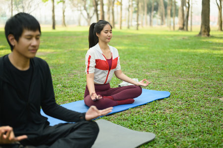 Young couple meditating peacefully in a green park, focus on breathing and stillness.の写真素材