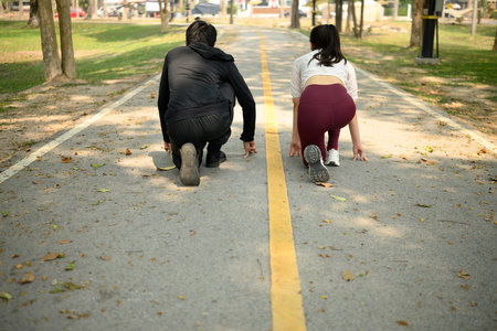 Young couple preparing to sprint in a park, crouched in starting position on a pathway.の写真素材