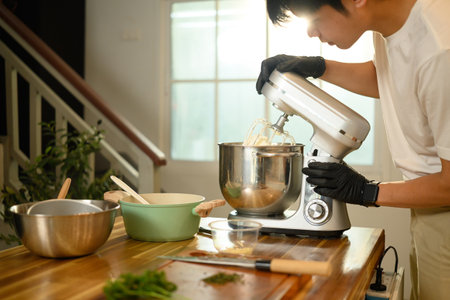 Young asian man using stand mixer to make whipped cream in a modern kitchen.