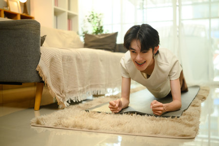 Cheerful young man doing a plank exercise on a yoga mat at home.の写真素材