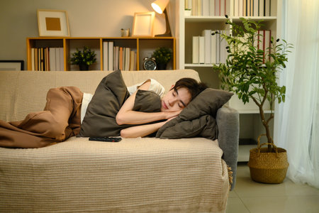 Young man peacefully napping on cozy sofa in warmly lit living room.の写真素材