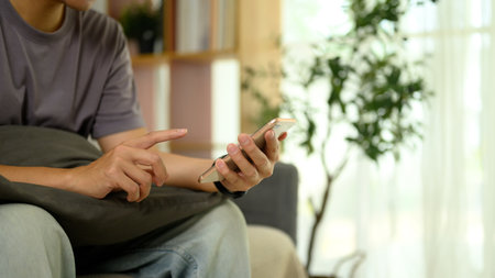 Cropped shot of young man in casual clothes using smartphone on sofa at home.