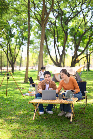 Happy couple using laptop while camping with their daughter in the background.の写真素材