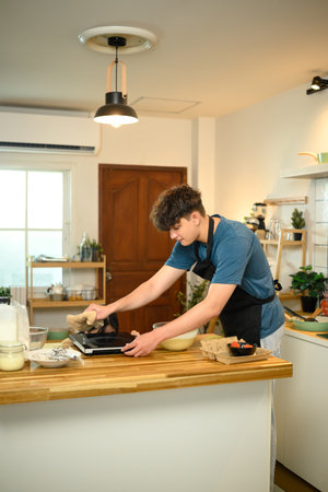 Man using electric griddle to make pancakes in cozy kitchen.の写真素材