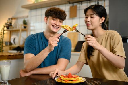 Happy young couple enjoying pancakes with strawberries and syrup in cozy home kitchen.の写真素材