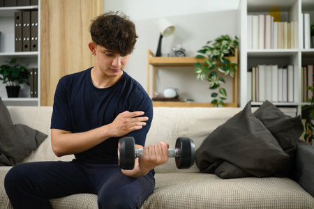 Young man lifting dumbbells on a sofa. Fitness at home concept.の写真素材