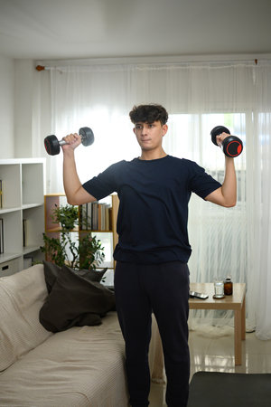 Young man lifting dumbbells at home during a strength training workout.の写真素材