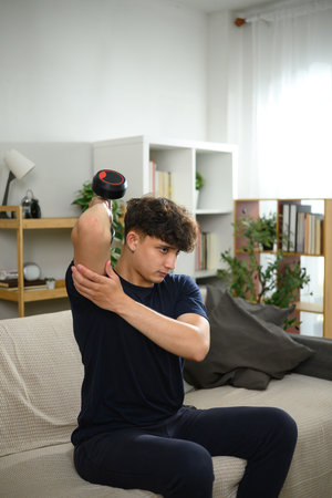 Young man lifting dumbbells on a sofa. Fitness at home concept.の写真素材