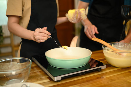 Close up of couple adding butter to pan while preparing pancake batter in kitchen.の写真素材