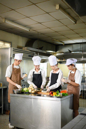 Young chefs practice slicing vegetables during a hands on cooking class at culinary school.の写真素材