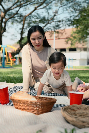 Mother and young child relaxing on picnic blanket in the park, enjoying a sunny day together.の写真素材