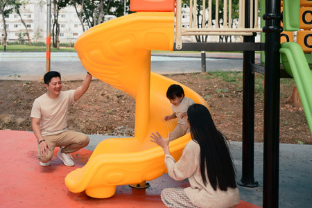 Happy parents playing with their young child at the playground slide on a sunny day..の写真素材