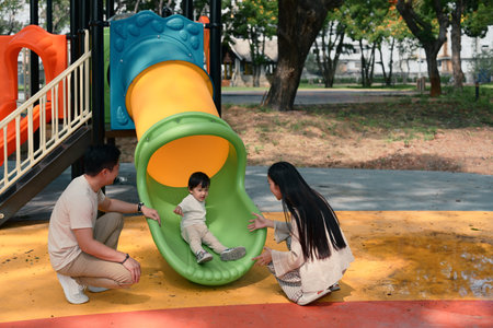Happy parents playing with their young child at the playground slide on a sunny day..の写真素材