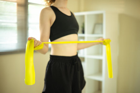 Active woman using resistance band for arm exercises in a bright living room.の写真素材