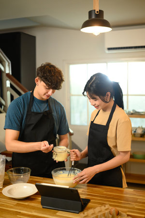 Cheerful young couple preparing breakfast pancakes in cozy home kitchen.の写真素材