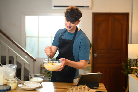 Cheerful man blending ingredients for pancakes, creating a homemade breakfast.の写真素材