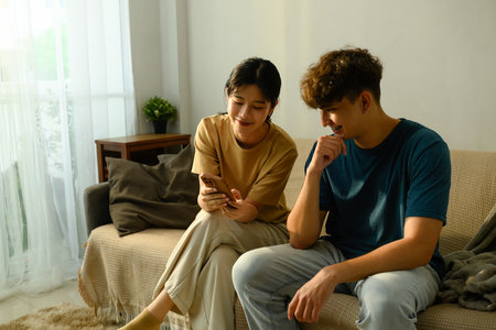 Relaxed couple sitting on couch together and looking at a mobile phone in a living room.の写真素材