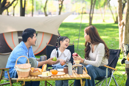Parents and joyful daughter having a relaxing outdoor meal during family camping trip in nature.の写真素材