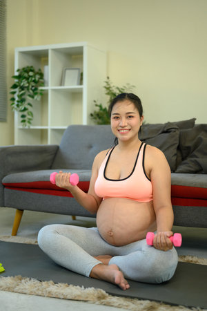 Pregnant woman working out indoors with small dumbbells.の写真素材
